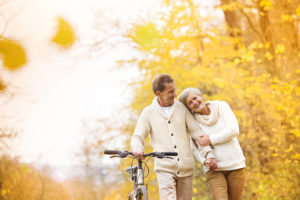Active senior couple together enjoying romantic walk with bicycle in golden autumn park